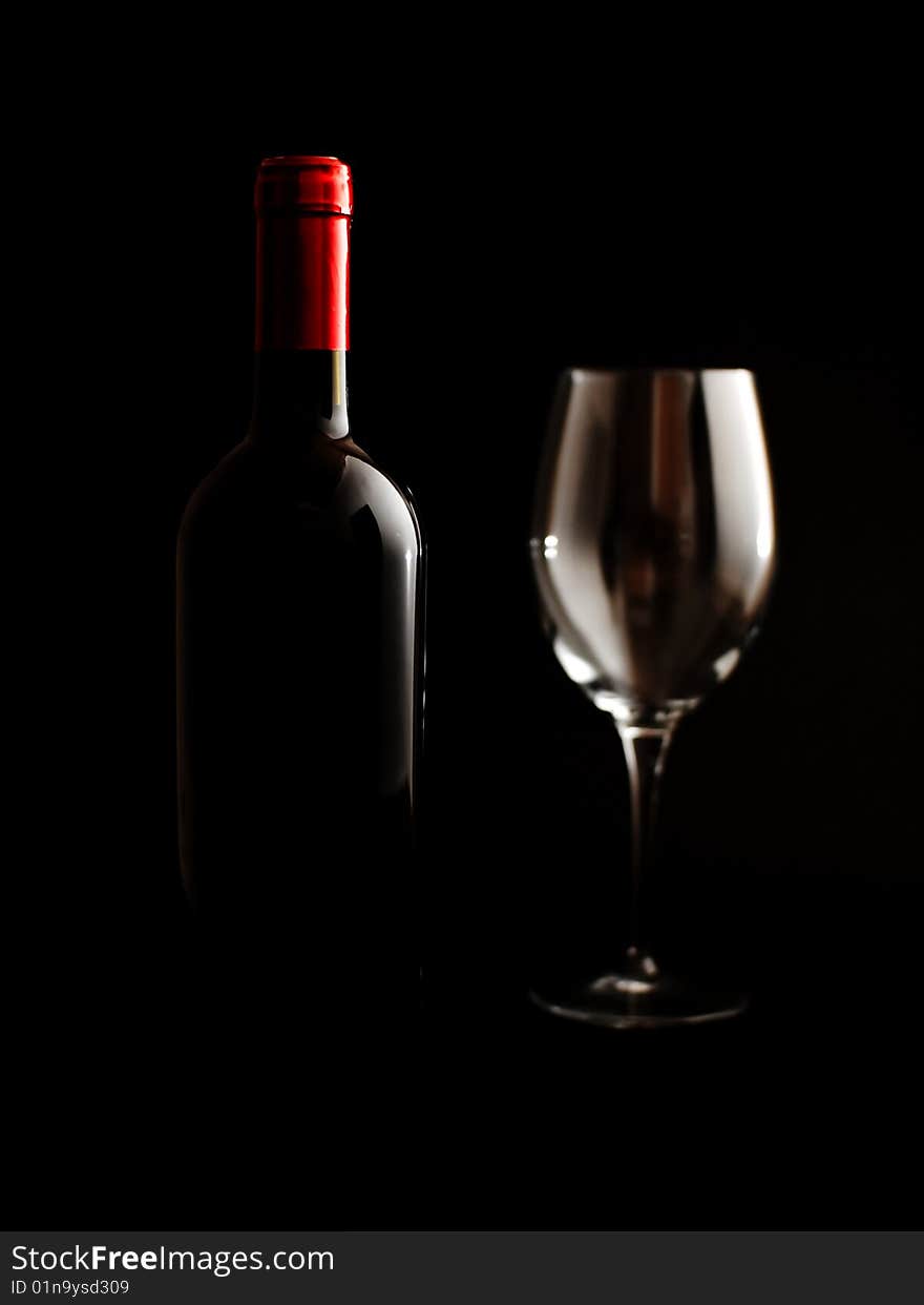 A wine bottle and an empty glass on a dark background. A wine bottle and an empty glass on a dark background.