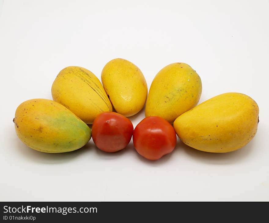 Yellow ripe mangoes and two tomatoes isolated over white background.