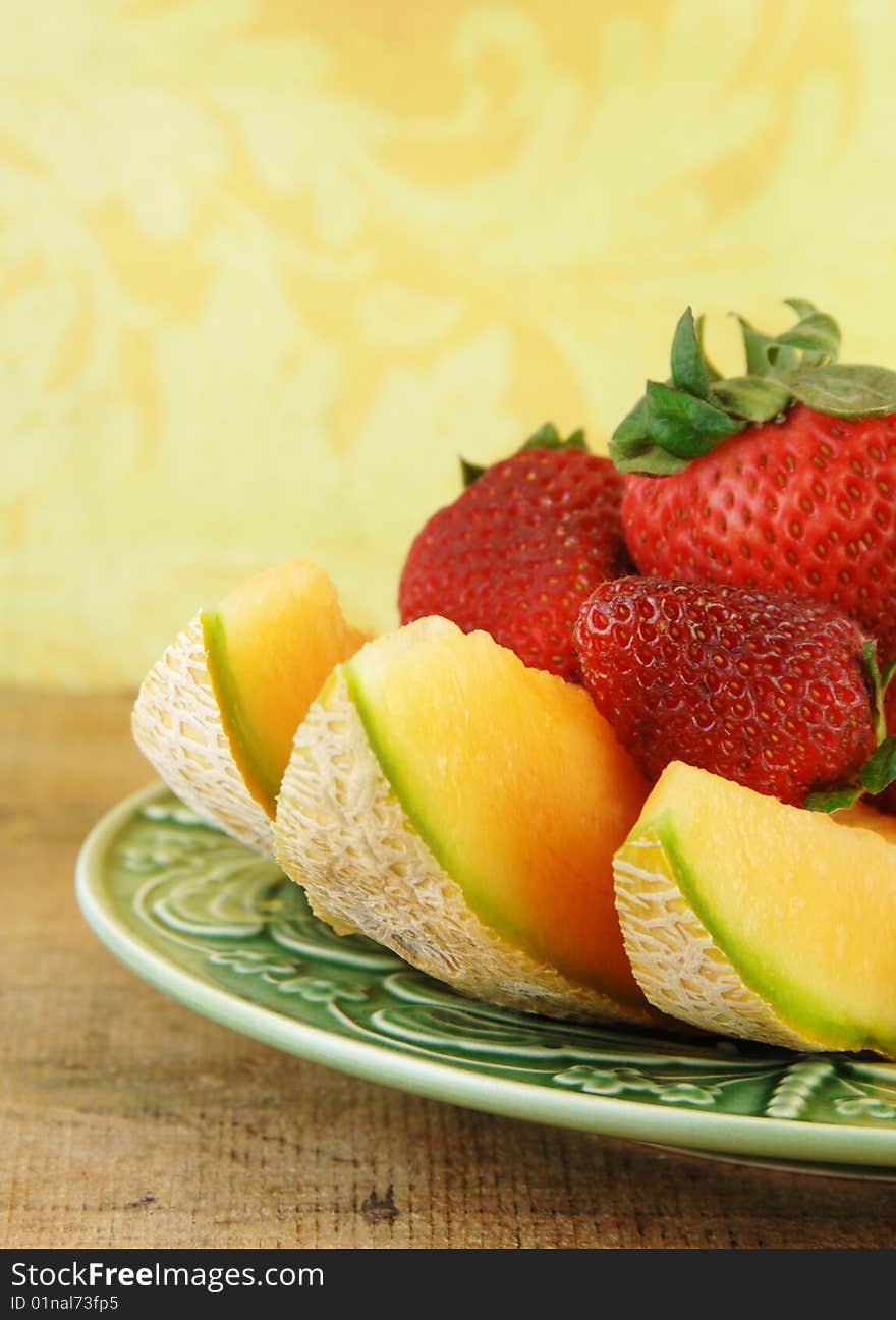 Sliced Cantaloupe and strawberries on a wooden table with a yellow background.