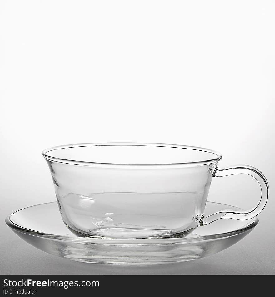 Glass teacup and a saucer on light background