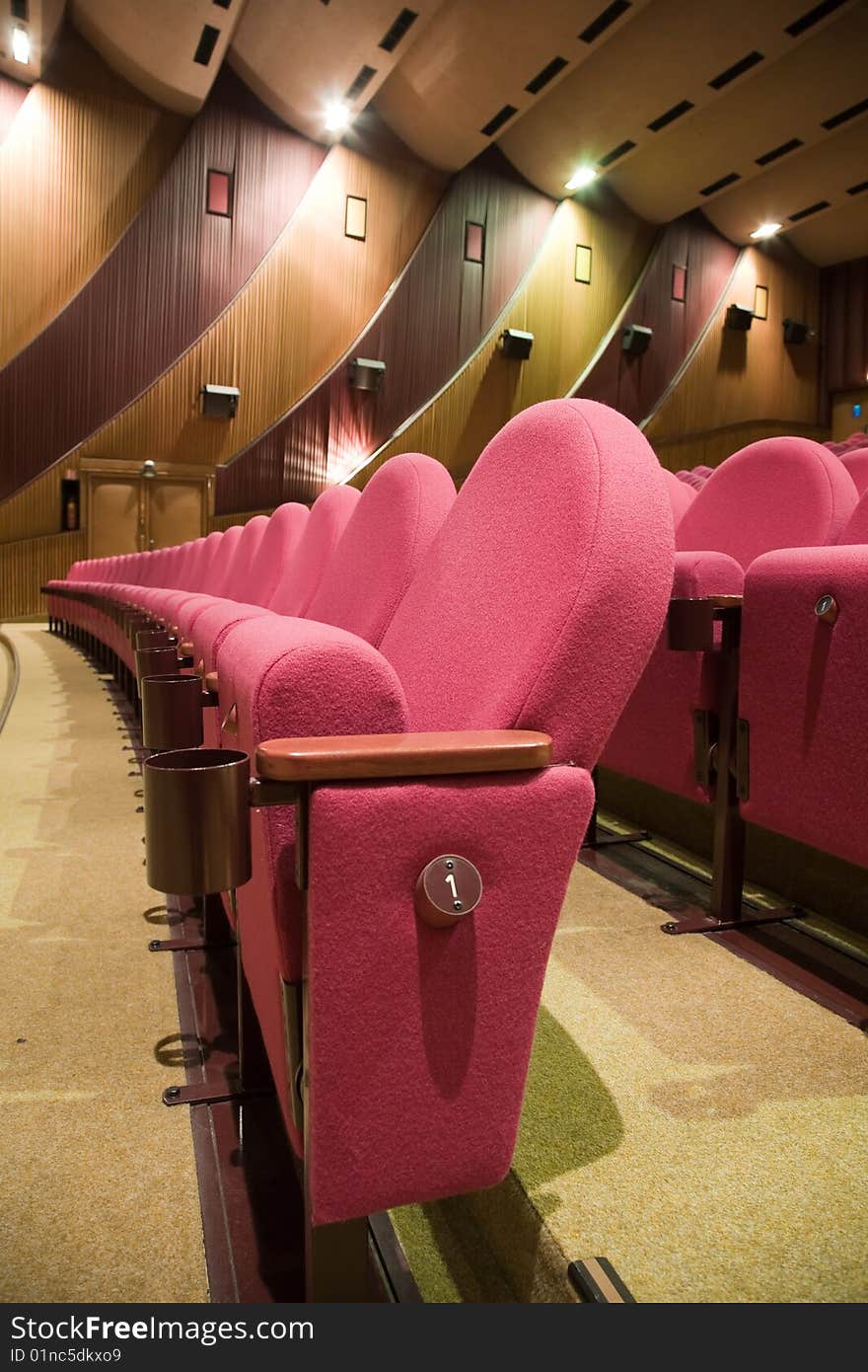 Pink row #1 of empty cinema auditorium with line of chairs.