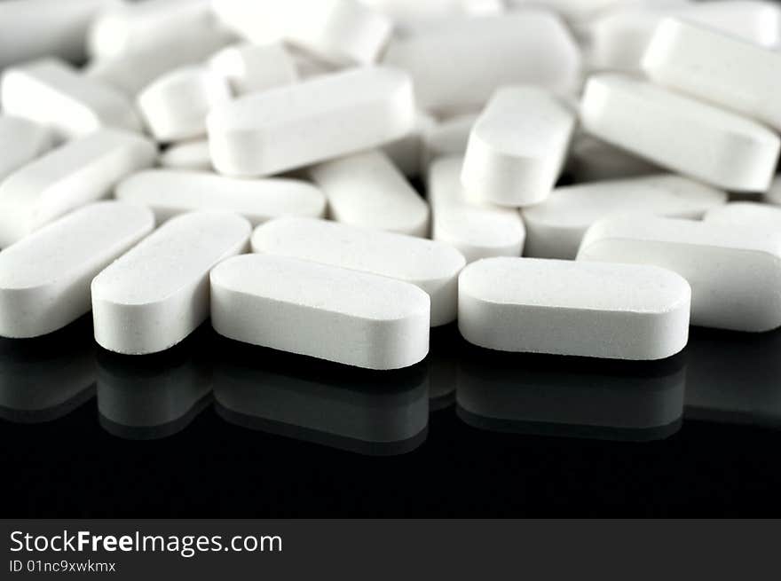 White medicine pills in big closeup with reflection at black background. White medicine pills in big closeup with reflection at black background