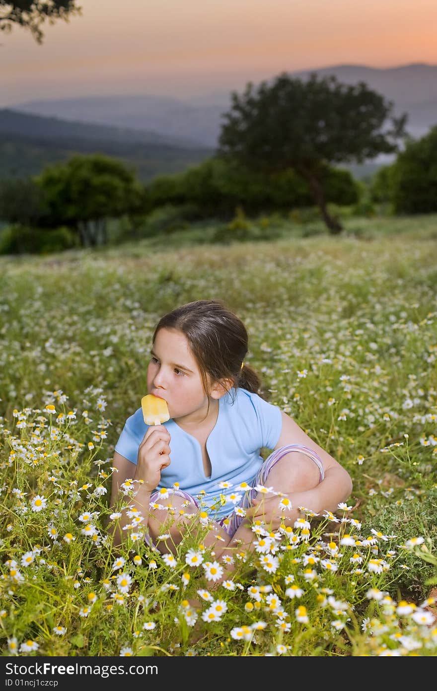 Young girl having a Popsicle in a flower field at sunset