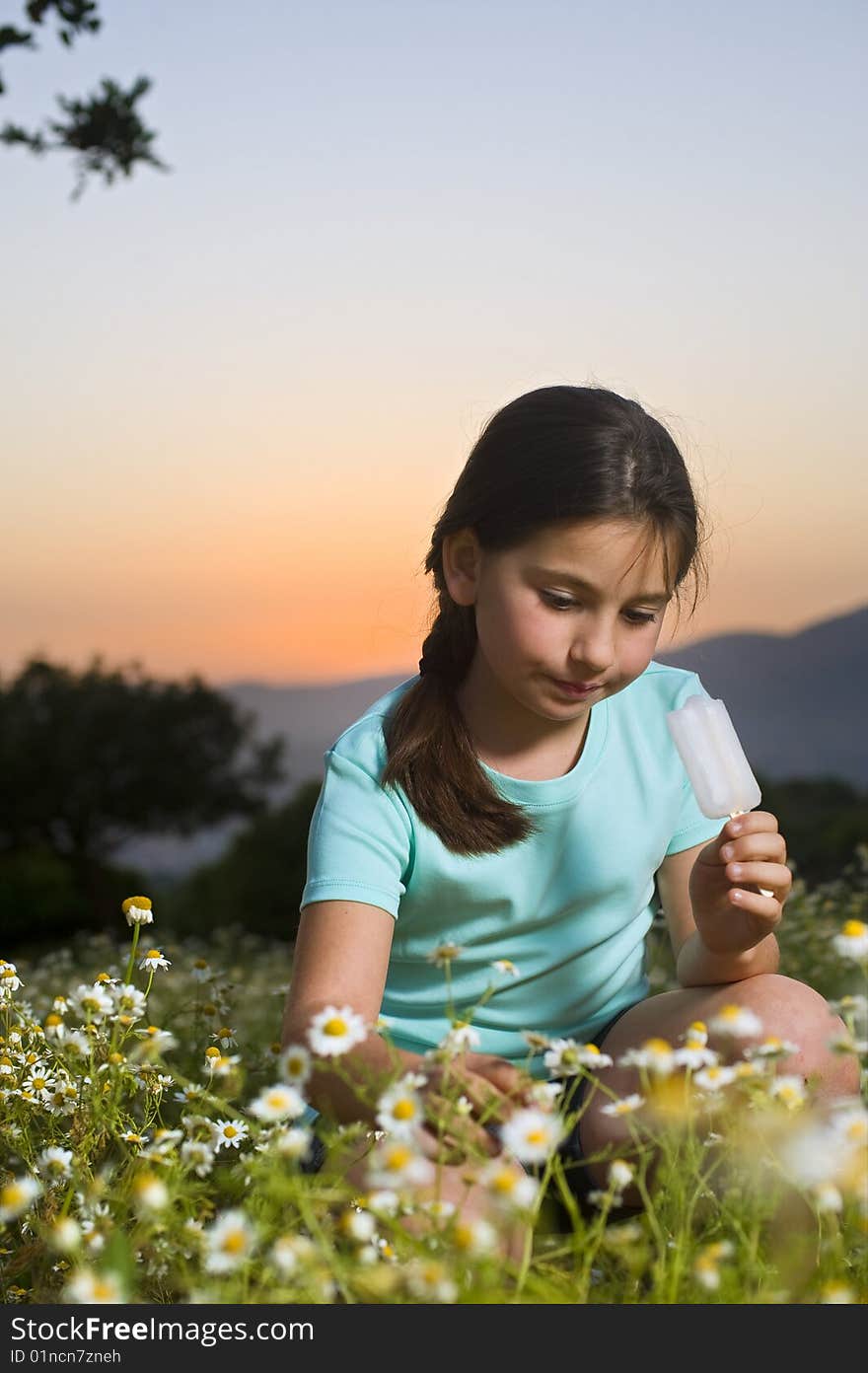 Young girl having a popsicle in a flower field at sunset