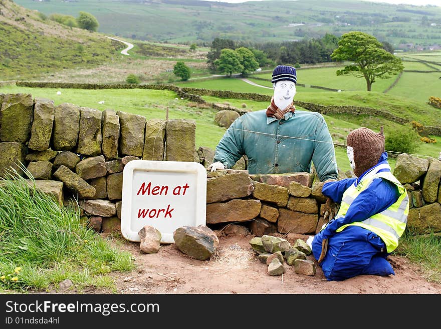 The photo shows scarecrow type representations of men building a wall. The photo shows scarecrow type representations of men building a wall