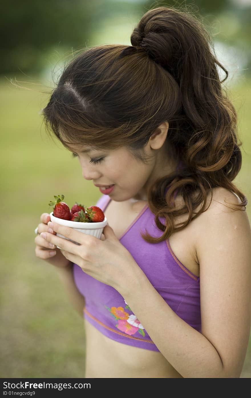 An asian lady taking a break enjoying a bowl of healthy strawberries.  She is enjoying the aroma from the bowl. An asian lady taking a break enjoying a bowl of healthy strawberries.  She is enjoying the aroma from the bowl.