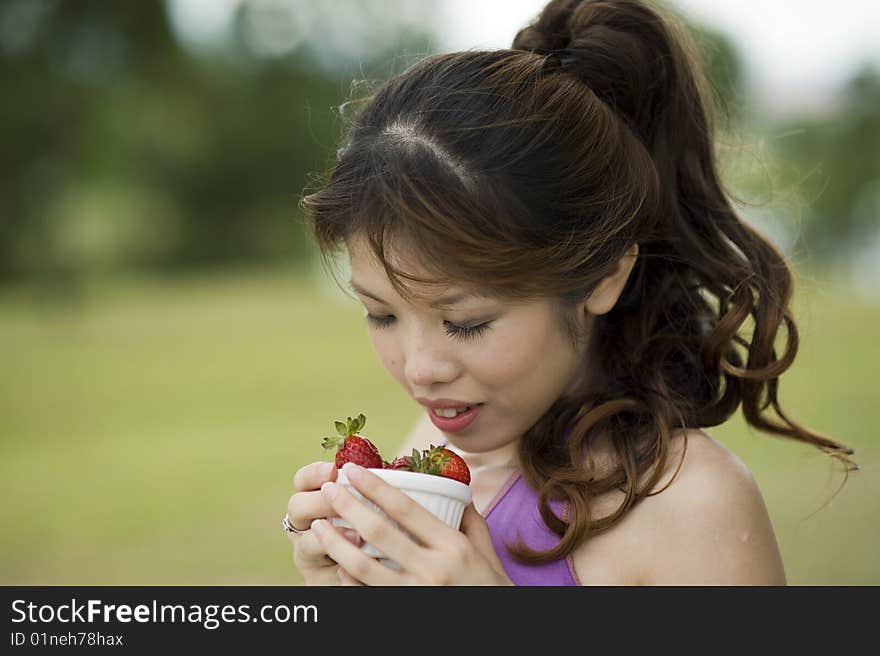 An asian lady taking a break enjoying a bowl of healthy strawberries.  She is enjoying the aroma from the bowl. An asian lady taking a break enjoying a bowl of healthy strawberries.  She is enjoying the aroma from the bowl.