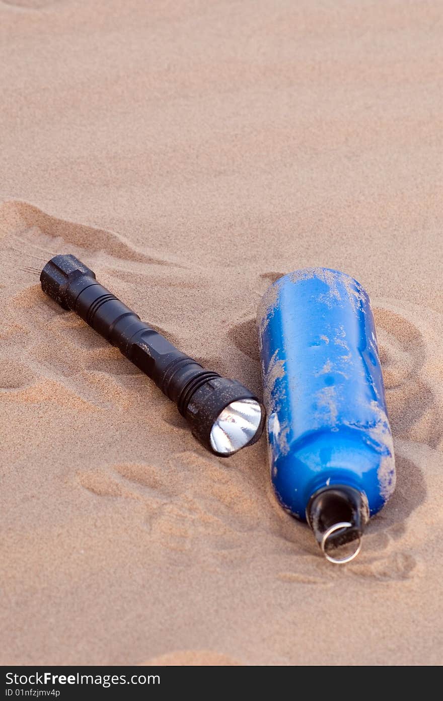 Sport bottle and flashlight in desert