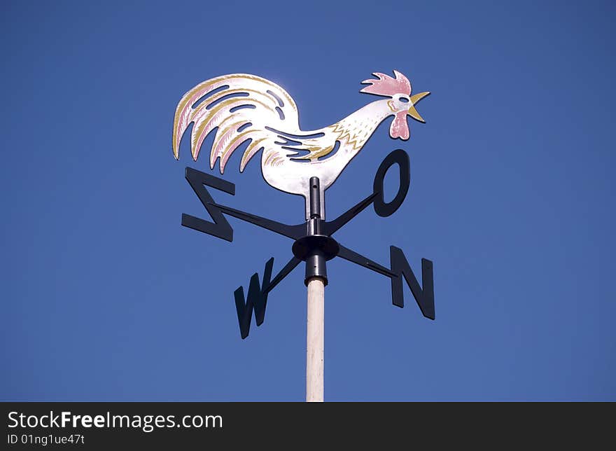 Weather vane - cockerel which reflected sun against bright-dark blue sky. Weather vane - cockerel which reflected sun against bright-dark blue sky