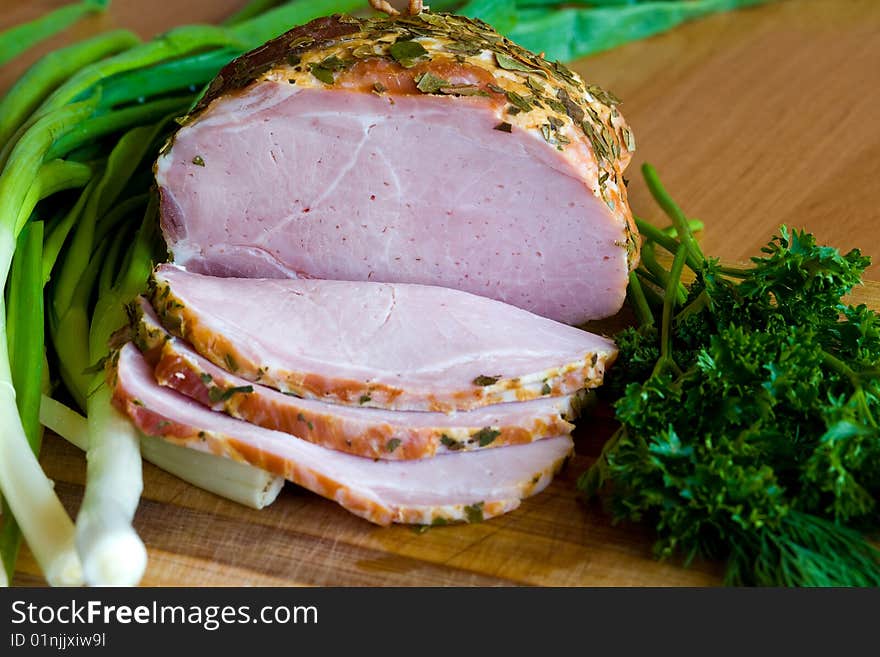 Appetizing slices of ham with potherbs on the kitchen table. Appetizing slices of ham with potherbs on the kitchen table