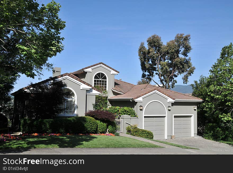 House surrounded by trees and blue sky. Split level with grass yard and shrubs.