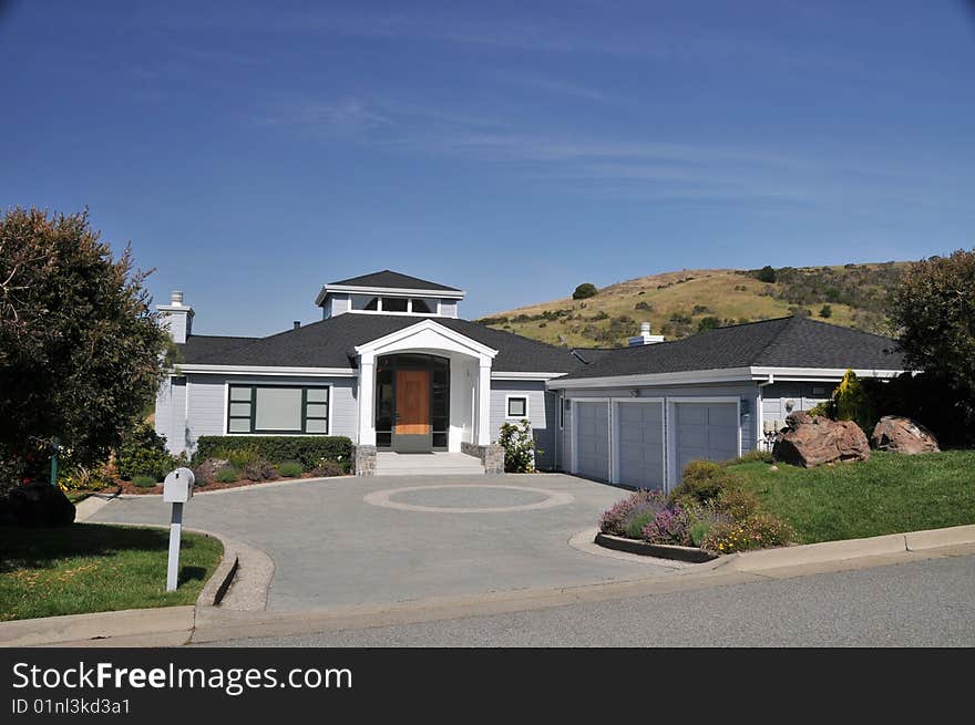 House with circular driveway for a three car garage. Blue sky. Grass yard and shrubs. Mountains in the background. House with circular driveway for a three car garage. Blue sky. Grass yard and shrubs. Mountains in the background.