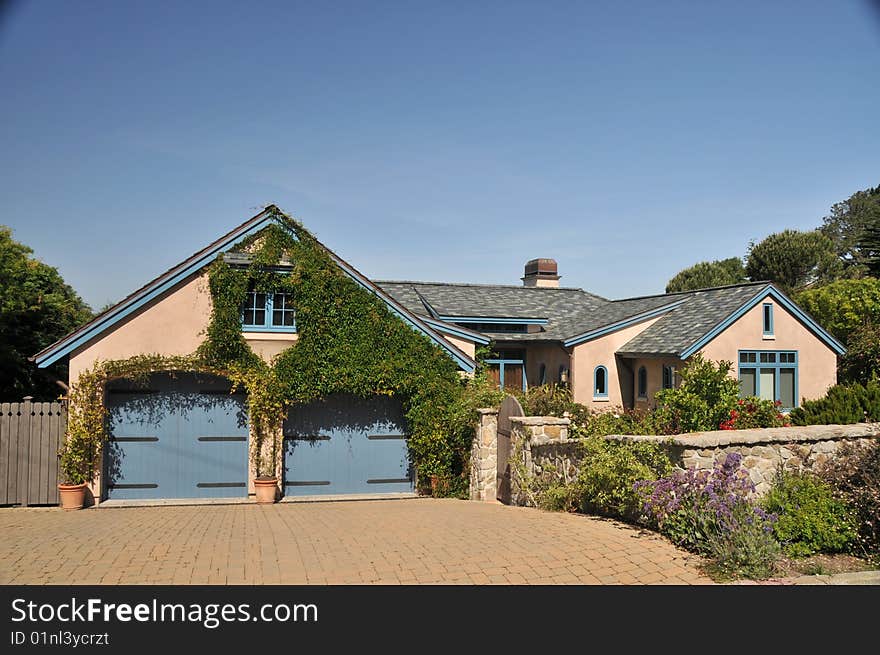 House with a two car garage with blue doors. Blue sky. Two levels. Rock fence enclosing yard. House with a two car garage with blue doors. Blue sky. Two levels. Rock fence enclosing yard.