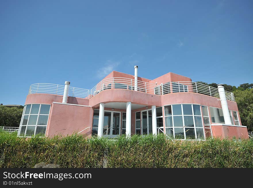 Pink two story house with white railings surrounded by green shrubs. Pink two story house with white railings surrounded by green shrubs.