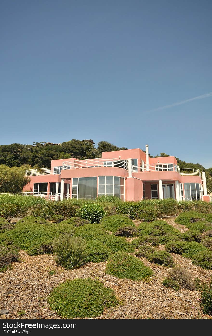 Pink two level house with shrubs in front. Lots of windows. Blue sky.