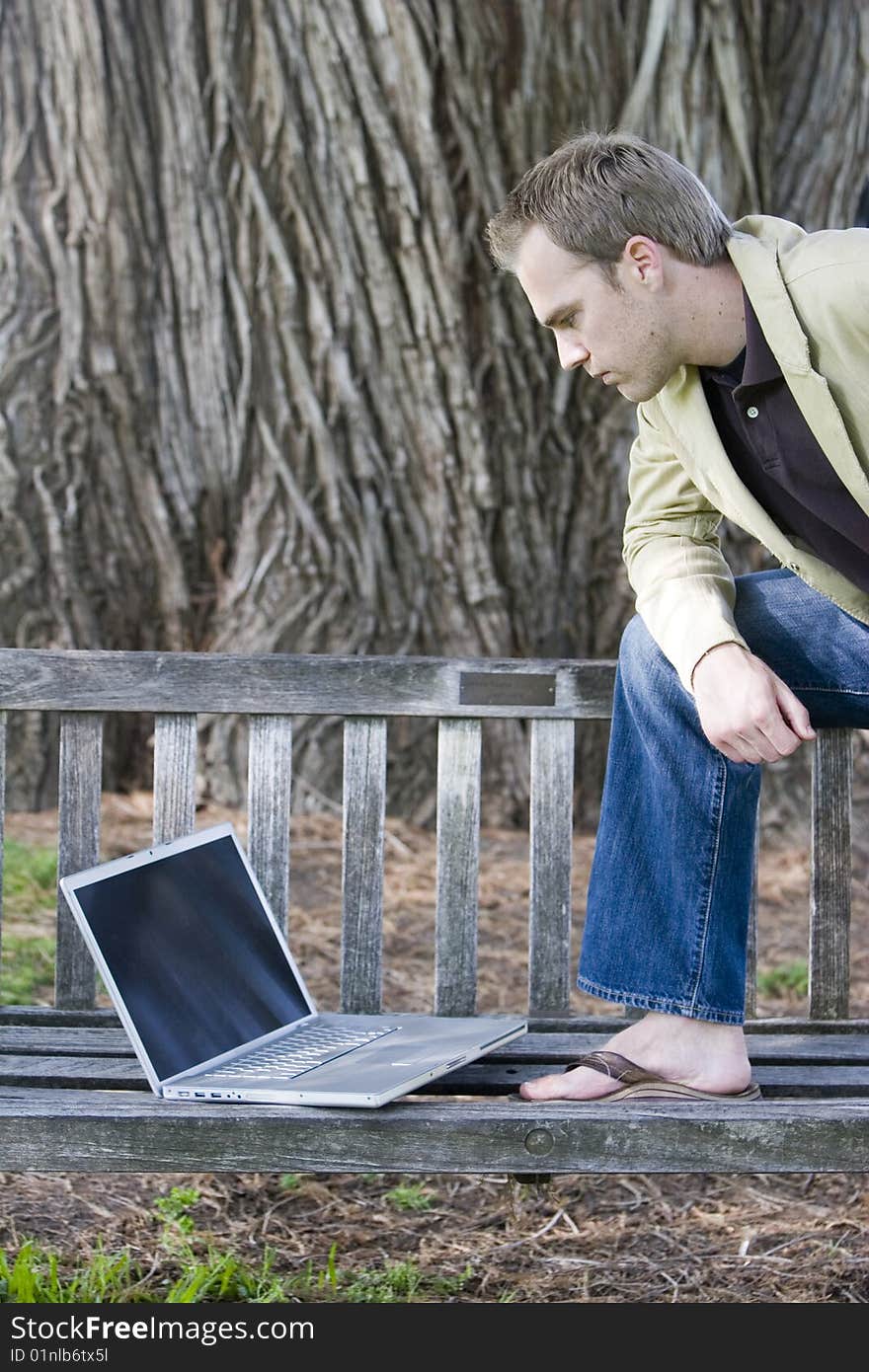 Young man studying a laptop computer on a park bench. Young man studying a laptop computer on a park bench