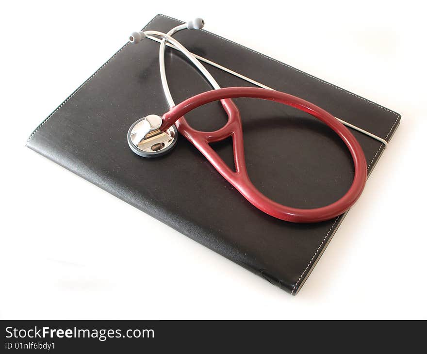 A maroon stethoscope on a black compendium isolated on white. A maroon stethoscope on a black compendium isolated on white