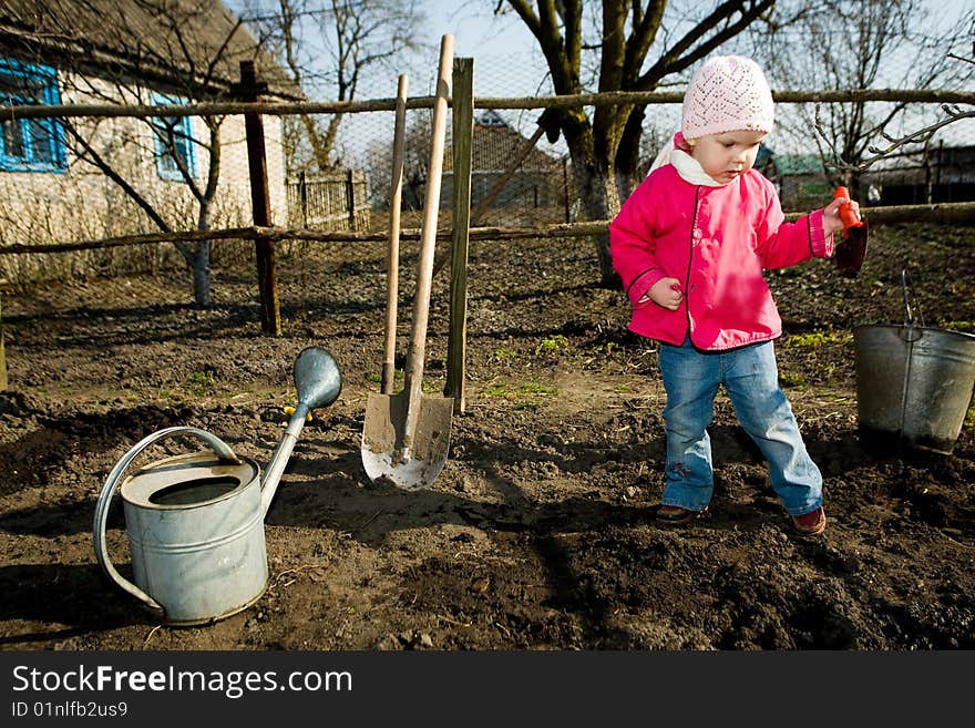 A pretty little girl  in  her grandfather's  kitchen garden  with  a toy  spade in  a hand. A pretty little girl  in  her grandfather's  kitchen garden  with  a toy  spade in  a hand