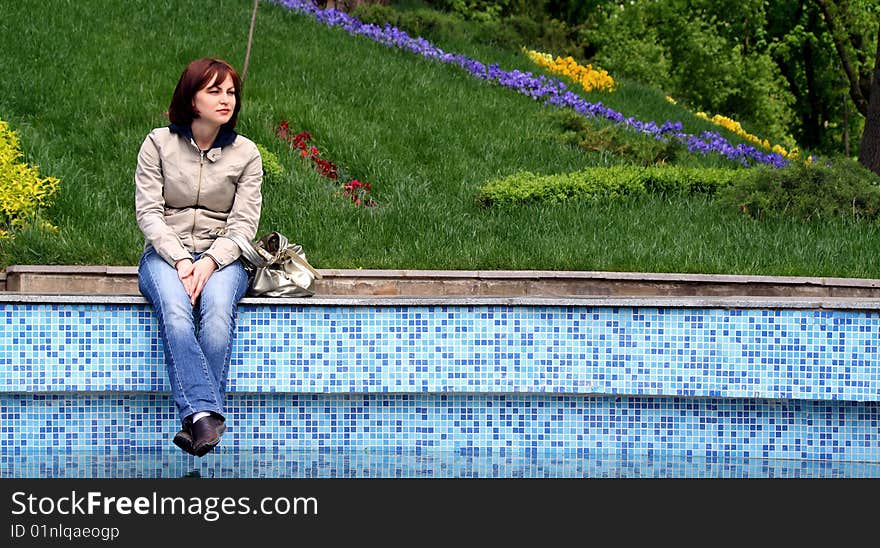 The girl near the pool, sat down to have a rest and look at floating birds. The girl near the pool, sat down to have a rest and look at floating birds