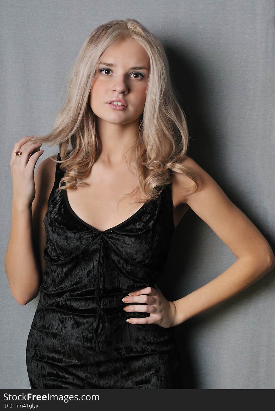 Portrait of a beautiful young girl in a black dress, standing on a gray background