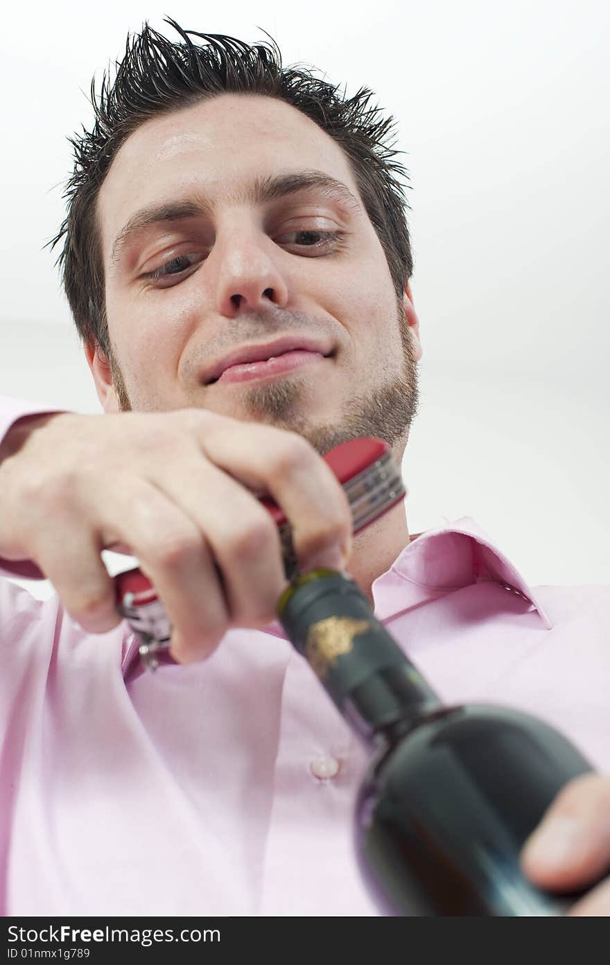 Young man, opening a bottle of red wine with cork screw, looking satisfied. Young man, opening a bottle of red wine with cork screw, looking satisfied