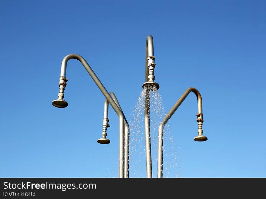 Four outdoor shower heads over deep blue and cloudless sky. Water leaking from one shower head. Green environment concept.