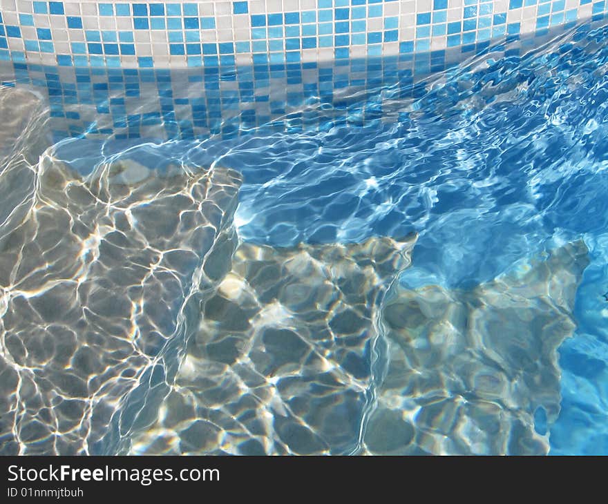 An image of steps going into a swimming pool with mosaic tiles around the edge. An image of steps going into a swimming pool with mosaic tiles around the edge