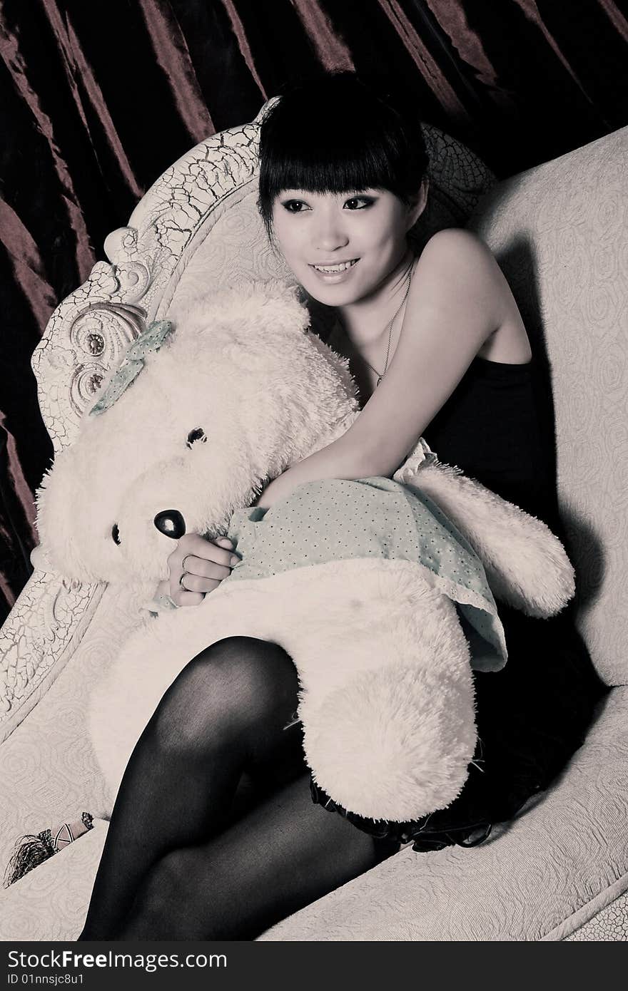 A beautiful Asian girl with teddy bear is watching television.