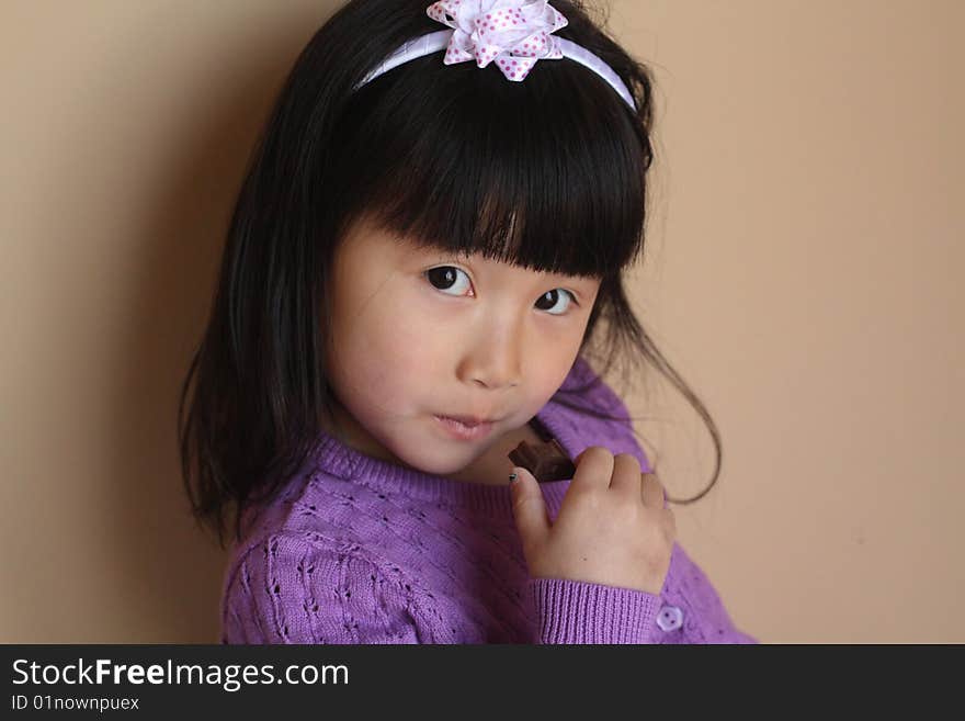 Asian Chinese Girl eating a small piece of chocolate with a head band with bow on top and purple sweater. Asian Chinese Girl eating a small piece of chocolate with a head band with bow on top and purple sweater