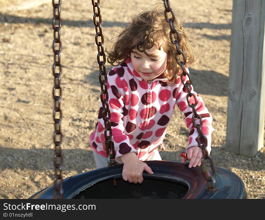 Young preschooler having fun at a playground with a tire swing suspended from chains. Young preschooler having fun at a playground with a tire swing suspended from chains.