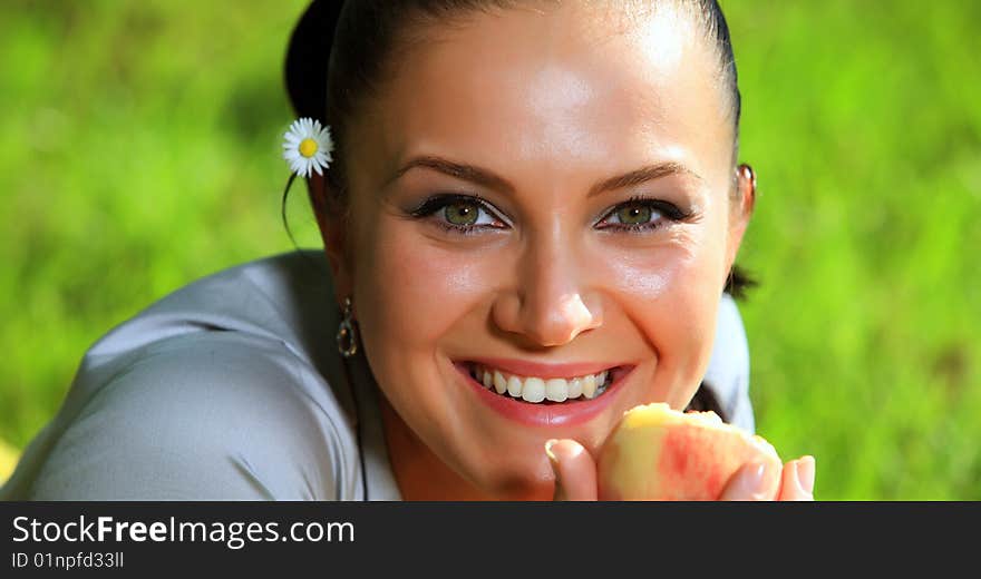 Attractive young girl is eating a fresh peach. She is lying on a nice fresh green grass meadow and smiling with a flower behind her ear. Attractive young girl is eating a fresh peach. She is lying on a nice fresh green grass meadow and smiling with a flower behind her ear