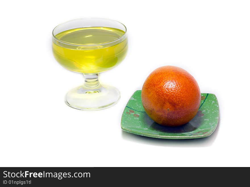 Yellow jelly but transparent glass and orange on green saucer on white background