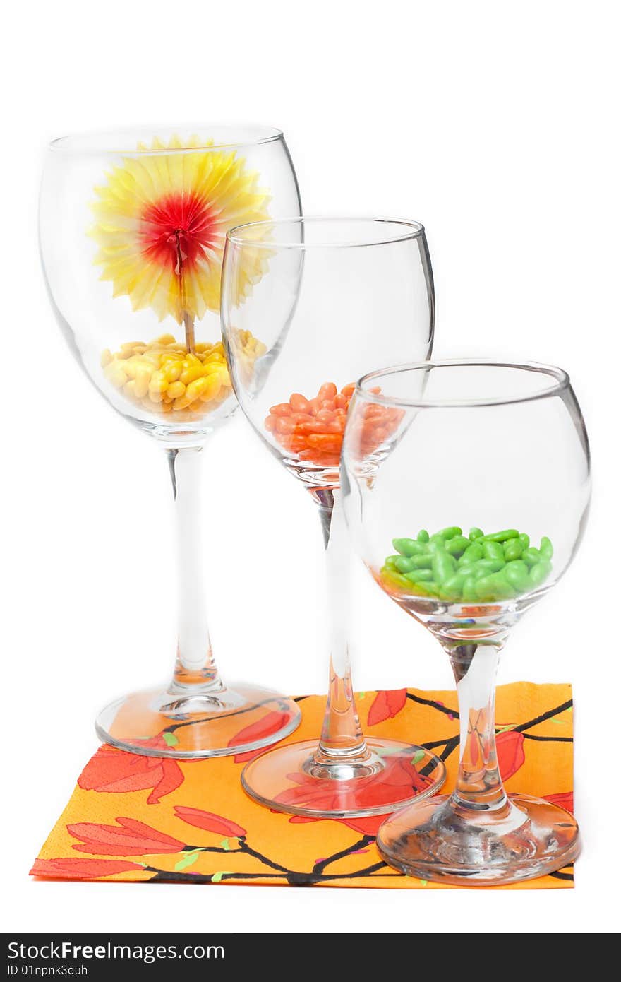 Three glasses with colour sweetmeat stand on orange napkin insulated on white background