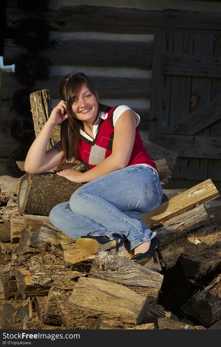 Teenager sits on pile of logs outside cabin. Teenager sits on pile of logs outside cabin.