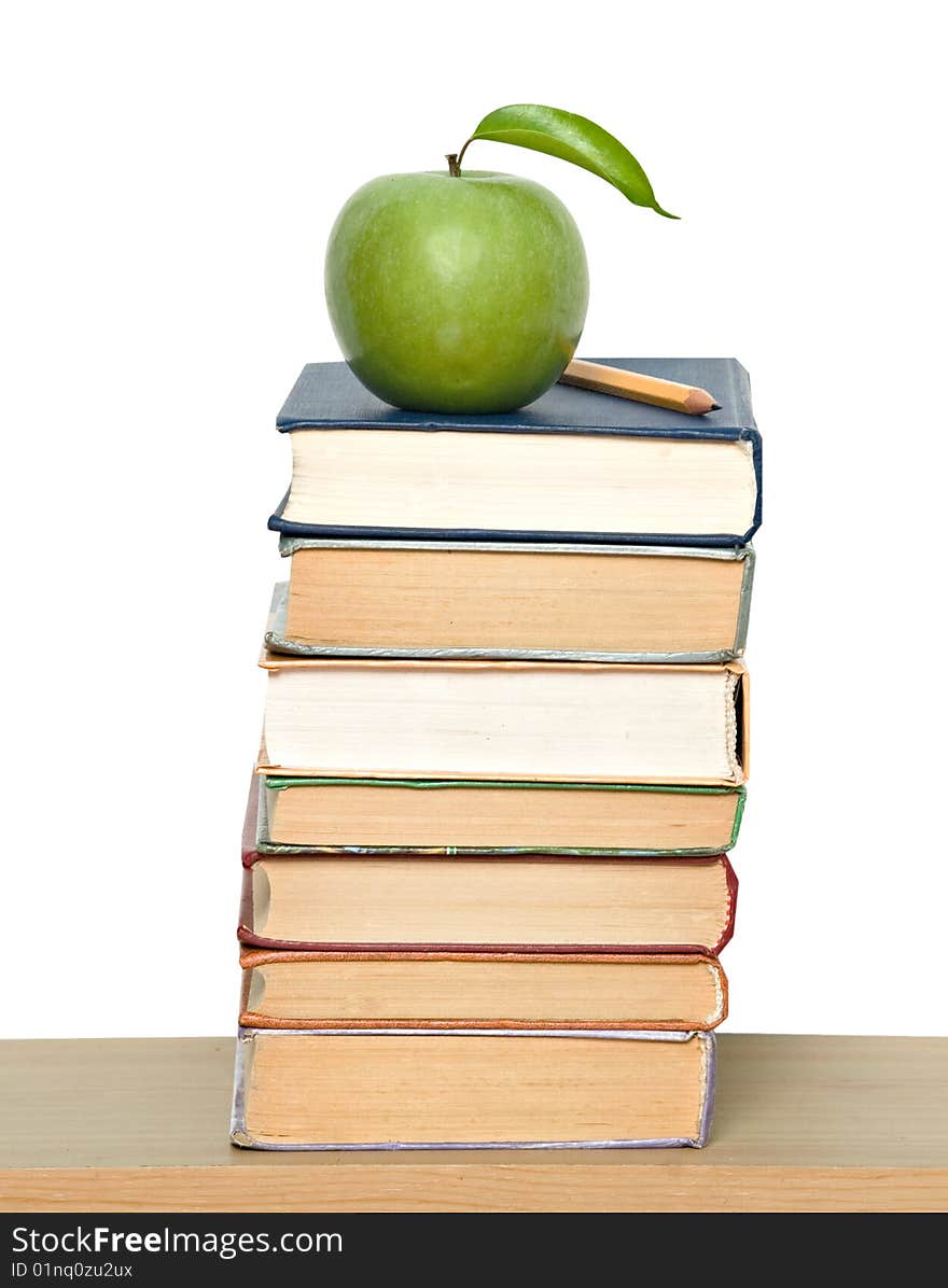 Green ripe apple and pencil on pile of books