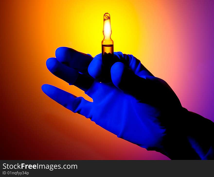 Gloved hand holding an clear ampule with liquid. Abstract circular background. Gloved hand holding an clear ampule with liquid. Abstract circular background.