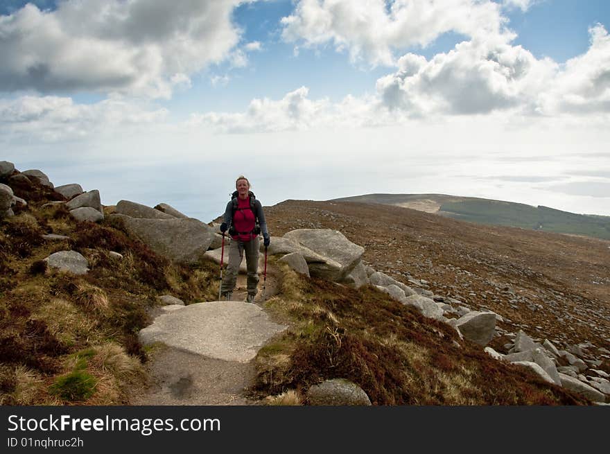 Woman walker with trekking poles on path in the mountains. Woman walker with trekking poles on path in the mountains