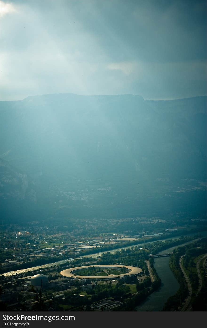 Image of a mountain valley with atmospheric lighting, and a view of the Grenoble particle accelerator (Cyclotron). Image of a mountain valley with atmospheric lighting, and a view of the Grenoble particle accelerator (Cyclotron).