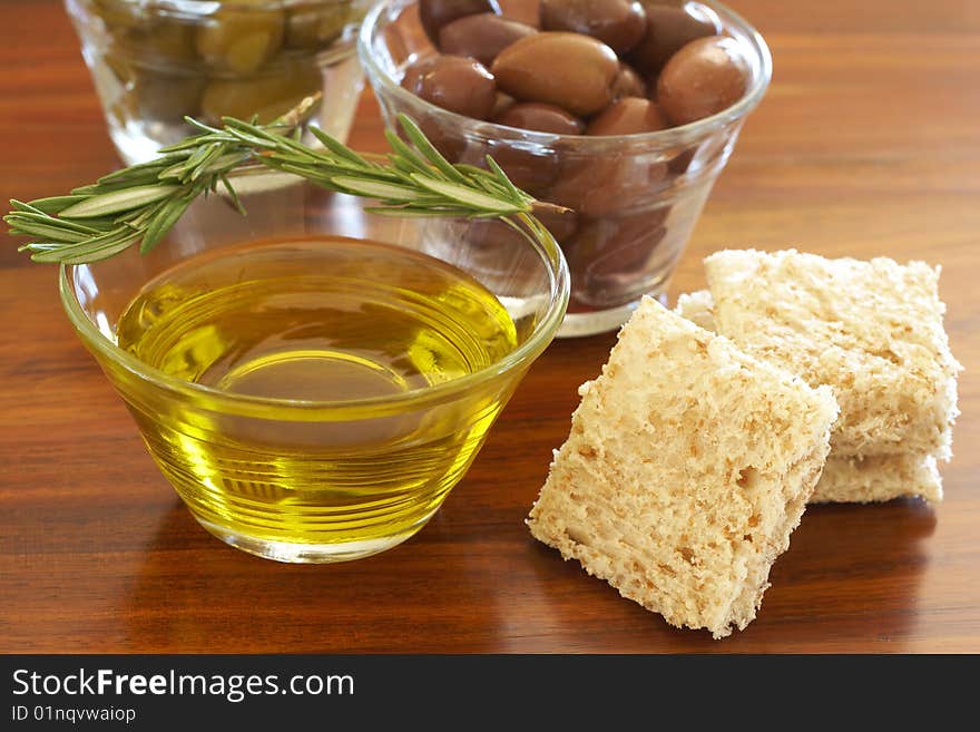 Two jars of green and black olives with stick of rosemary, olive oil and slices of bread on wooden table background. Two jars of green and black olives with stick of rosemary, olive oil and slices of bread on wooden table background