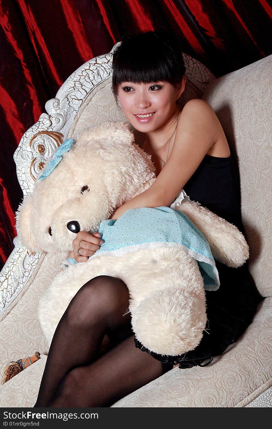 A Asian girl is holding the teddy bear and watching TV . A Asian girl is holding the teddy bear and watching TV .