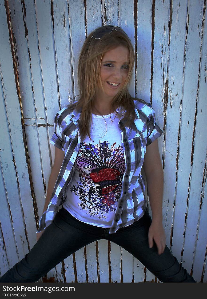 A white caucasian girl teenager with a happy expression on her face standing against a white fence. A white caucasian girl teenager with a happy expression on her face standing against a white fence