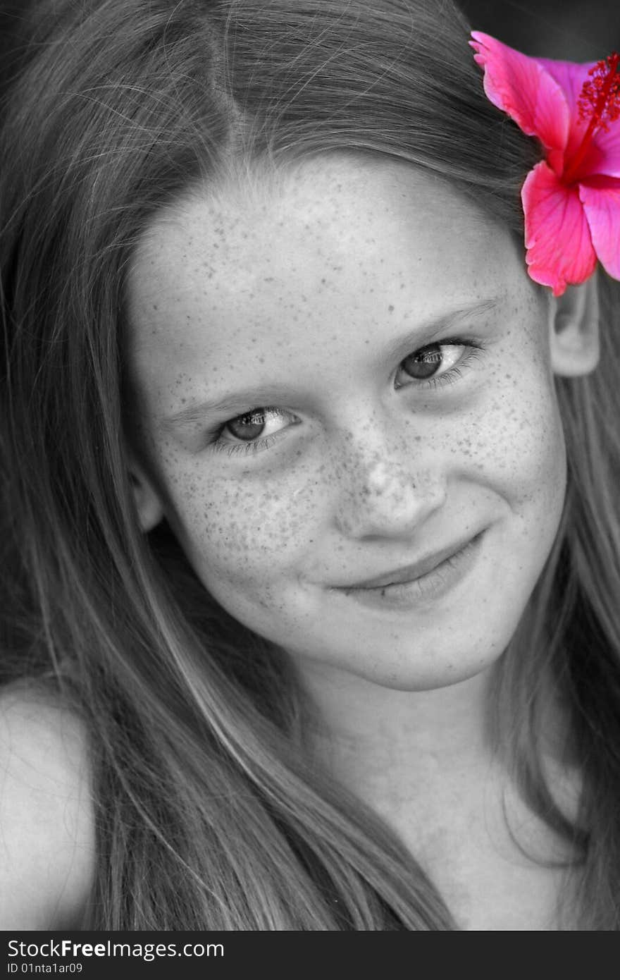 A white caucasian kid smiling with a flower in her hair. Picture in black and white with flower in pink. A white caucasian kid smiling with a flower in her hair. Picture in black and white with flower in pink