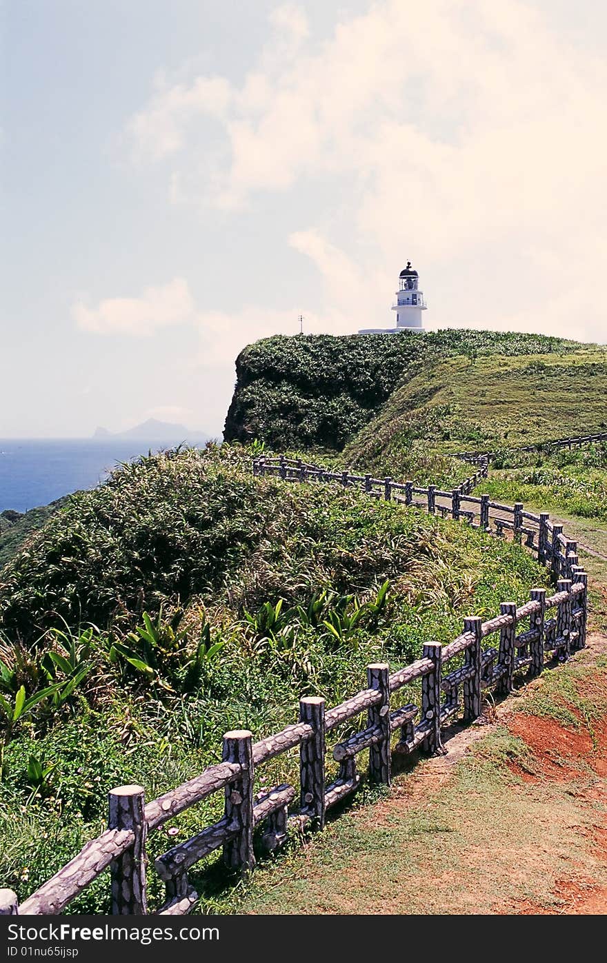 A trail leads to a lighthouse on a hill by the sea. A trail leads to a lighthouse on a hill by the sea