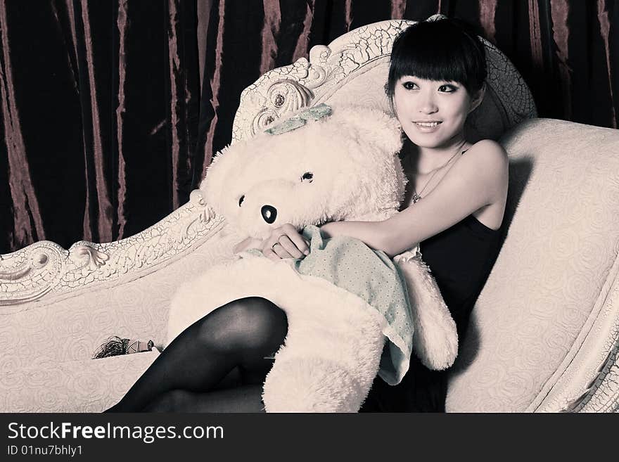 A Asian girl is holding the teddy bear and watching TV . A Asian girl is holding the teddy bear and watching TV .