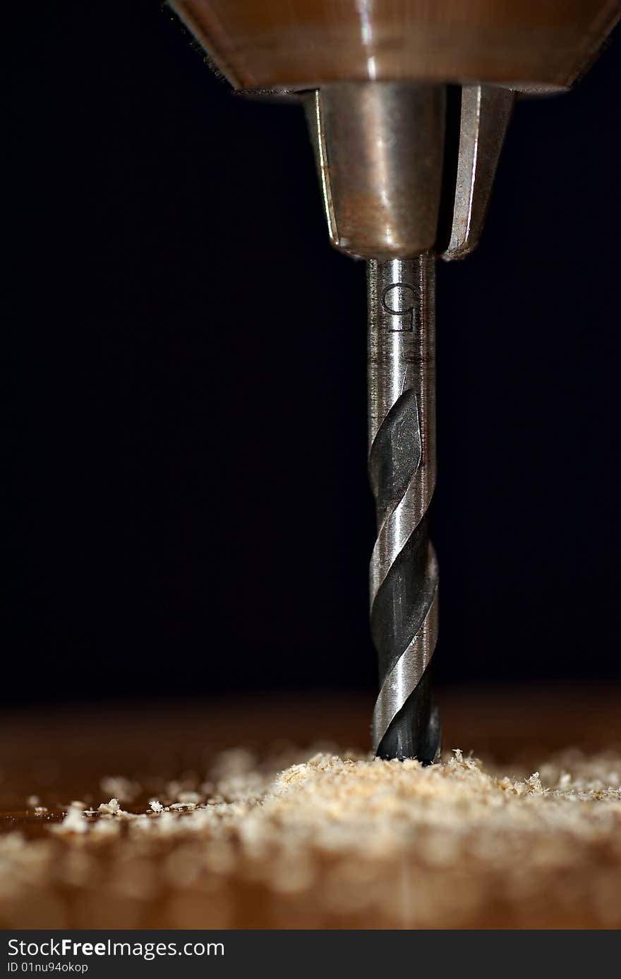 Detail of  drill bit in a piece of wood with dark background