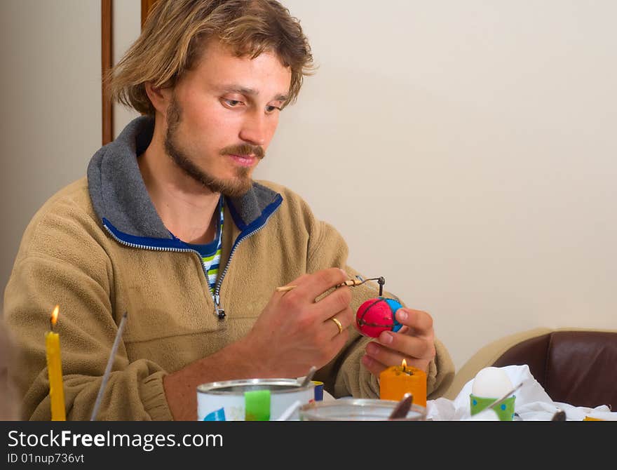 Man painting Easter egg with technique of wax putting