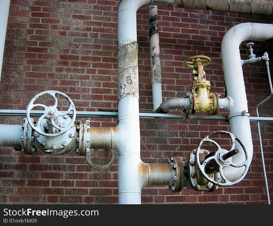 Old blue valves and piping in an abandoned chemical plant against a red brick wall. Old blue valves and piping in an abandoned chemical plant against a red brick wall.