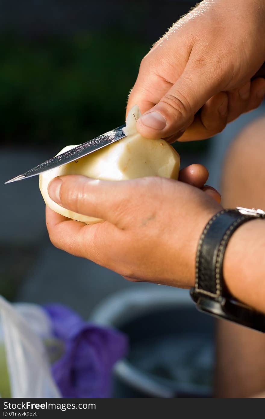 Men's hands with a knife clean potatoes.