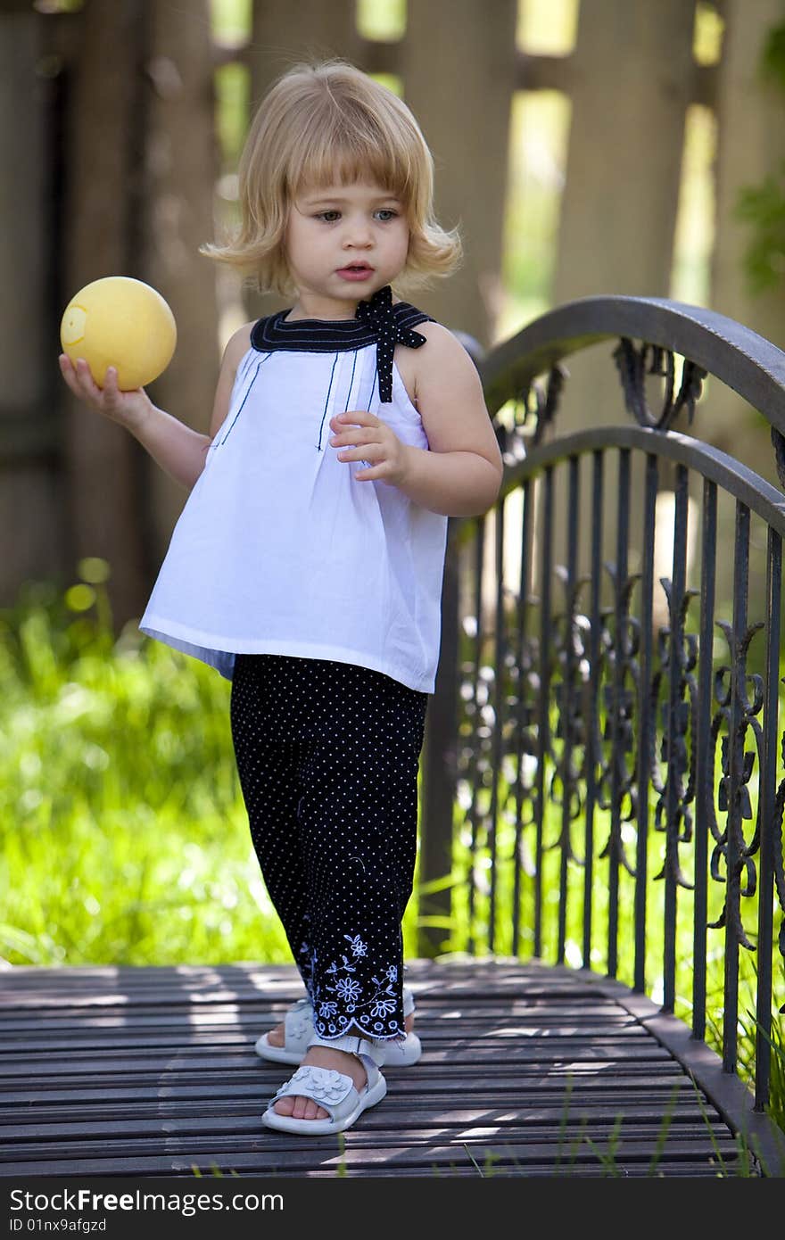 Little girl standing on bridge with yellow ball in her hand. Little girl standing on bridge with yellow ball in her hand