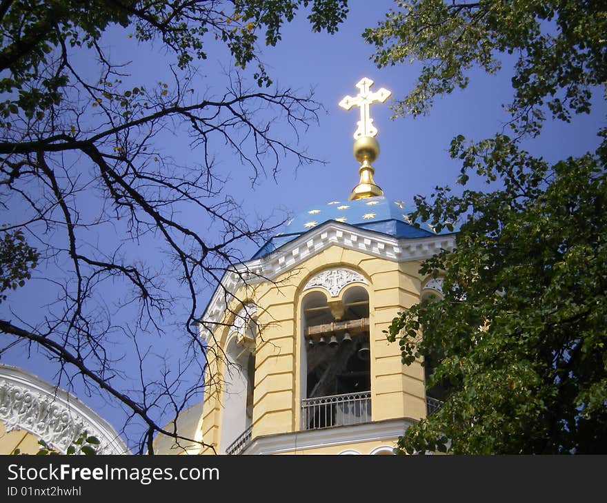 Dome of cathedral with a shining gold cross in framing of dry branches and silhouettes of leaves of chestnut. Dome of cathedral with a shining gold cross in framing of dry branches and silhouettes of leaves of chestnut